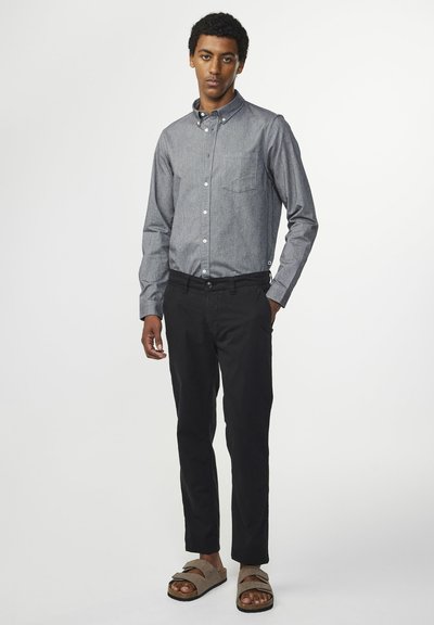 Herre skjorte med knapper i mørkegrå chambray, parret med sorte slim-fit bukser og brune sandaler med brede stropper.