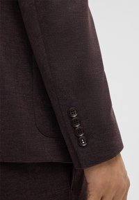 Manica di blazer viola scuro con tessuto testurizzato, quattro bottoni scuri e polsino ben rifinito.