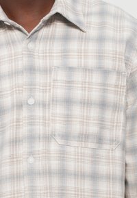 Koszula w kratę w jasnym beżu i niebieskich odcieniach, z zapięciem na guziki z przodu, spiczastym kołnierzykiem oraz kieszenią na piersi o subtelnej fakturze.