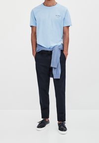 Himmelblå bomulds t-shirt med korte ærmer og sort tekst. Mørkeblå bukser og en lys blå sweater bundet omkring taljen. Sorte sneakers.