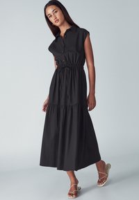 Čierne midi šaty s krátkymi pufovanými rukávmi, s predným zapínaním na gombíky, elastickým pásom a tiered lemom. Hladký materiál a voľný strih. Elegantné sandále.