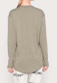 Långärmad skjorta i khakifärgad tyg, med rundad fåll och avslappnad passform. Mjuk textur med minimala sömmar och inga synliga mönster.