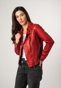 Veste de motard en cuir rouge avec une finition texturée, des poches zippées, des boutons-pression et une coupe légèrement ajustée. Portée par-dessus un haut blanc.