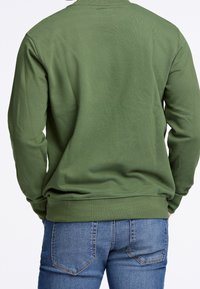 Felpa verde in cotone con maniche lunghe e girocollo, abbinata a jeans di denim blu con tasche posteriori e design aderente.