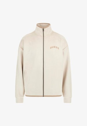 Beige vetoketjutakki, jossa on stand collar, sivutaskut, ribbed hihansuut ja "GUESS"-logo vasemmassa rinnassa.