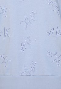 Světlá modrá tkanina s opakovanými vyšitými abstraktními symboly "A|X" ve shodné nitce, žebrovaný lem dole.