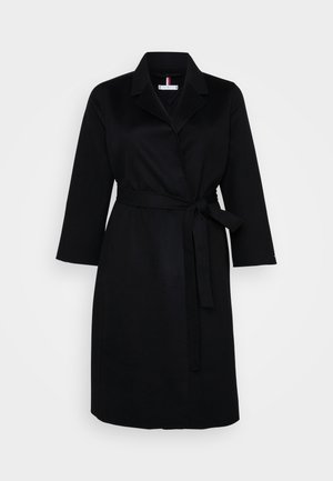 Cappotto nero avvolgente con colletto a punta, maniche lunghe e cintura da annodare in vita; realizzato in un tessuto liscio con una texture uniforme.