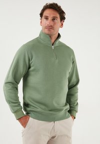 Green zip-neck sweatshirt made of textured fabric, featuring long sleeves and a relaxed fit. The design includes ribbed cuffs and hem.