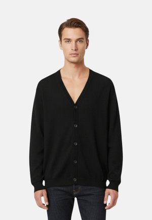 Uomo che indossa un cardigan nero con scollo a V abbottonato, maniche lunghe e jeans scuri, in piedi davanti a uno sfondo bianco uniforme.
