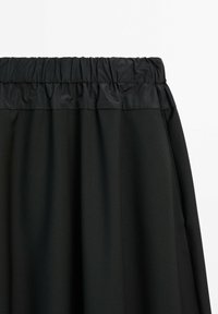 Gonna nera con vita elasticizzata arricciata. Realizzata in un tessuto leggero e liscio con un design semplice e fluente.