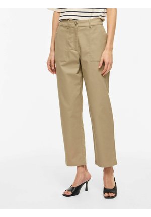 Kvinne iført beige bukser med rette ben og frontlommer, sammen med svarte åpen-tå heeled mules, kombinert med en stripete topp som er stukket inn.