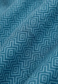 Tela azul con patrón que presenta un diseño geométrico de cuadrados y rombos entrelazados. La textura parece suave y tejida.