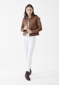 Brun läderkort jacka med krage, två framfickor, silvriga tryckknappar. Tillsammans med vita jeans och bruna ankelskor.