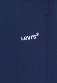 Levi's tamnoplavi materijal pokazuje meku teksturu s bijelim vezom logotipa. Dizajn je jednostavan i minimalizam, s naglaskom na detalj logotipa.