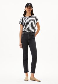 Schwarze, hochtaillierte Jeans aus Denim, kombiniert mit einem schwarz-weißen gestreiften T-Shirt und beigen Slippern, ergänzt durch eine schwarze Mütze.