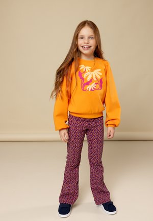 Oranje sweatshirt met bloemdruk, gecombineerd met paarse flared pants met patroon. Schoenen zijn marineblauw met witte zolen. Soepele stoftextuur.