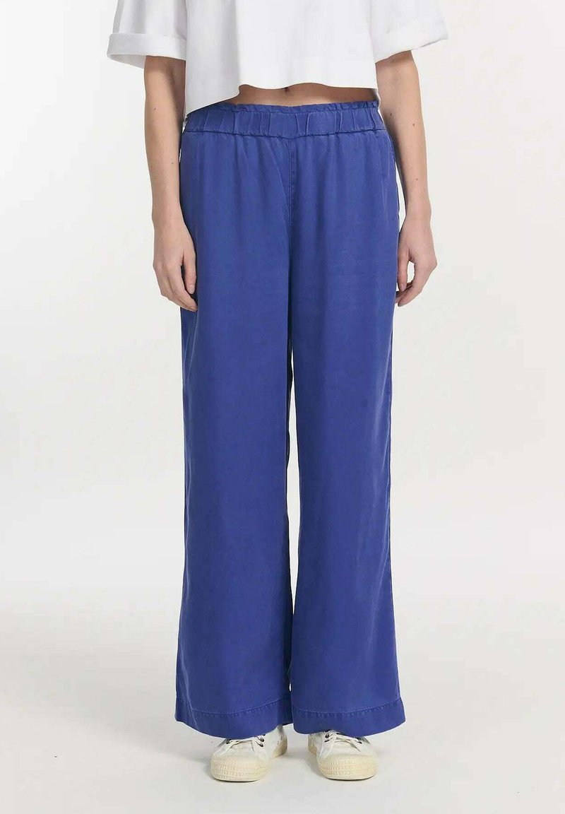 Blauwe wijde broek met een elastische tailleband, gemaakt van lichte stof. De broek heeft een zachte textuur en valt tot de enkels.