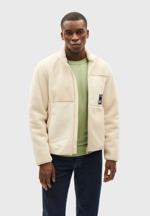 Fleecejacke in Creme mit Reißverschluss vorne und strukturierter Oberfläche, ausgestattet mit einer Brusttasche und einem kontrastierenden, weich grünen Innenfutter.