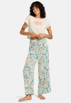 Ingekorte lichtbeige t-shirt met roze logo; losse, wijde broek met een pastel bloemenpatroon in blauw en roze en een elastische tailleband.