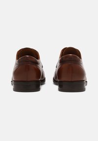 Des chaussures habillées en cuir marron avec une finition lisse, un bout rond et un petit talon noir. Elles présentent des coutures minimales et un design épuré.