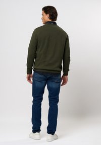 Grønn genser med ribbestrikkede mansjetter og krage, kombinert med blå jeans. Antrekket har et uformelt design og hvite sneakers.