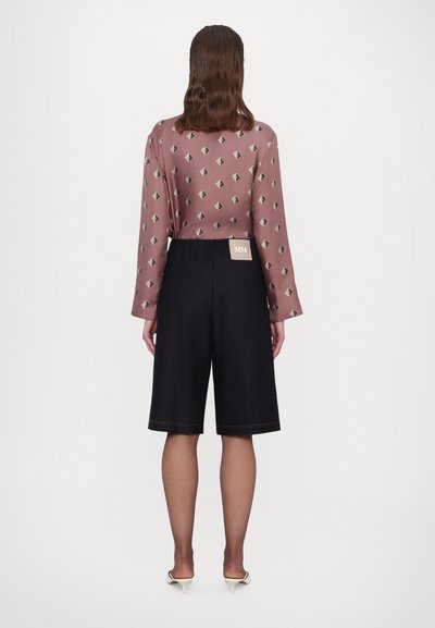 Pitkähihainen mauve-paita, jossa on timanttikuvio; yhdistetty tummiin farkkushortseihin ja vaaleansinisiin korkokenkiin. Brändilappu näkyy shortseissa.