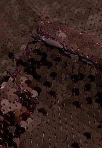 Sötét flitteres szövet, kerek, fényes flitterekkel, melyek különböző burgundi és bordó árnyalatokban tündökölnek, szorosan rétegzett textúráért és fényességért.