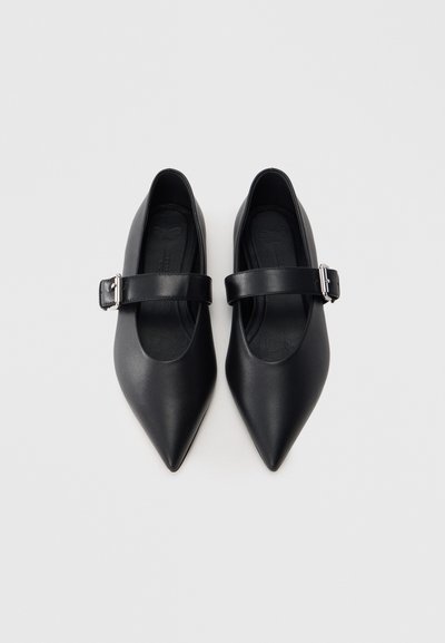 Μαύρα μπαλαρίνια με μυτερή μύτη από λείο δέρμα. Διαθέτουν λεπτή λουρίδα με ασημένια πόρπη πάνω από το πάνω μέρος του ποδιού. Μινιμαλιστικός σχεδιασμός.