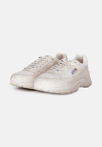 Scarpe da ginnastica beige con tomaia in pelle texturizzata, dettagli in rete e una spessa suola in gomma con un motivo in rilievo. Design con lacci e dettagli del logo.