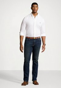 White collared shirt, dark blue jeans, brown belt, and brown shoes; relaxed fit with button-up design and rolled sleeves.