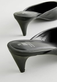 Juodi aukšti kulniukai mules su lygiu odiniu paviršiumi, apvaliu pirštu ir elegantišku stiletą kulnu. Tekstūruotas padas su ženklinimu.