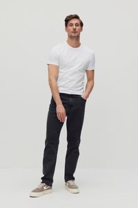 Witte T-shirt met ronde hals in combinatie met donkere spijkerbroek. Model draagt beige en grijze sneakers. Recht modelontwerp met minimale details.