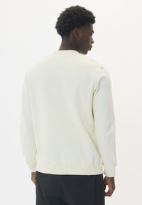 Crèmekleurige sweatshirt, zachte stof, ronde halslijn, lange mouwen, ribgebreide boorden en zoom, gladde textuur, minimalistisch ontwerp.