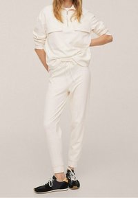 Sudadera cremosa con cremallera y dos bolsillos delanteros combinada con pantalones jogger a juego con cordón. Zapatillas negras con cordones blancos y detalles en color tostado.