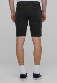 Shorts in denim nero, a vestibilità slim, lunghezza a metà coscia, design a cinque tasche, cuciture in evidenza e un accessorio a catena sulla vita.