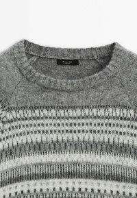 Pull en maille grise avec un col rond arborant un motif fair isle blanc et gris foncé sur la poitrine et les manches.
