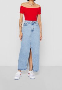 Rød off-the-shoulder top parret med en lyseblå denim maxi-nederdel med en frontspalt. Båret med hvide sneakers.