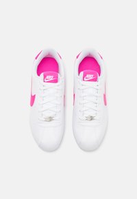 Pár fehér Nike sneaker élénk rózsaszín részletekkel, beleértve a pántot, a belső bélést és a nyelv logóját, felülnézetből mutatva.