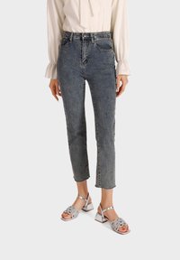 Jeans a vita alta dritti in denim blu sbiadito con due tasche frontali. Abbinati a sandali argento con cinturini decorati da fiori.