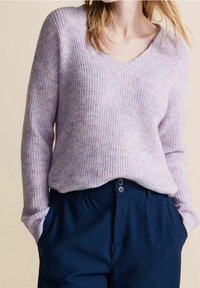 Light purple knitted sweater with a V-neck and ribbed texture, featuring soft, blended yarn. Paired with dark navy trousers.