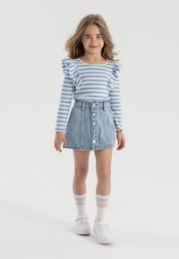 Modra in bela prugasta dolga majica z naborki na ramenskem delu, v kombinaciji s svetlim denim krilom z gumbom spredaj. Bele superge in prugaste nogavice.