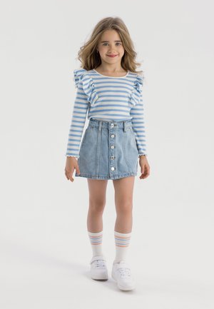Langärmliges Oberteil mit blauen und weißen Streifen und Rüschen an den Schultern, kombiniert mit einem hellen Jeansrock mit Knopfleiste. Weiße Turnschuhe und gestreifte Socken.