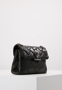 Svart läderhandväska med ett quiltat mönster, utrustad med ett spänne i silverton, kedjestrap och en dekorativ emblem på klaffen.