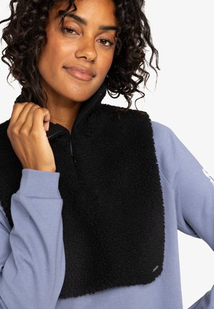 Cache-nez en polaire noire avec un col haut et une fermeture éclair. Porté sur une chemise à manches longues bleu clair, avec une texture douce.
