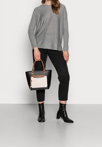Pull gris en maille avec manches longues, associé à un jean noir court. Sac cabas noir avec un accent beige et une poignée en bois. Bottines noires.