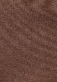 Tessuto marrone con una trama a tessitura diagonale, caratterizzato da una sensazione morbida e leggermente ruvida. Il colore è uniforme senza variazioni evidenti.
