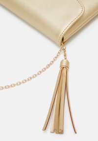 Clutch de cuero sintético dorado con una cadena desmontable y un adorno de borla hecho de tiras delgadas de cuero doblado en tonos dorados a juego.