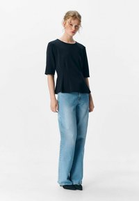 Zwarte top met korte mouwen en een ronde hals, gecombineerd met lichtblauwe wijduitlopende jeans. Gladde textuur, eenvoudig ontwerp zonder patronen.