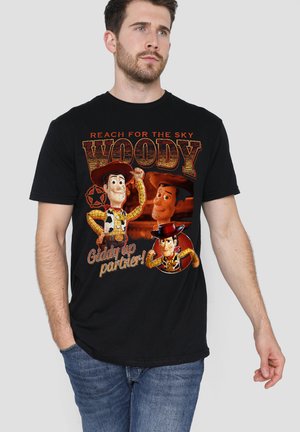 Man wearing black T-shirt with three Woody characters from Toy Story and text "Reach for the sky" and "Giddy up partner!"