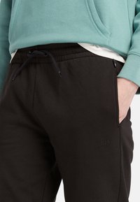 Pantalons de survêtement noirs en mélange de coton doux, dotés d'une taille élastique avec cordon de serrage, de poches latérales et d'un petit logo en relief.